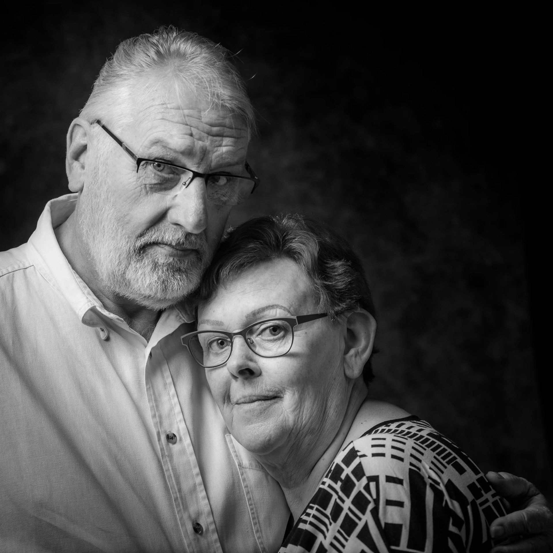 Een man en een vrouw poseren voor een zwart-witfoto. De vrouw draagt een bril.