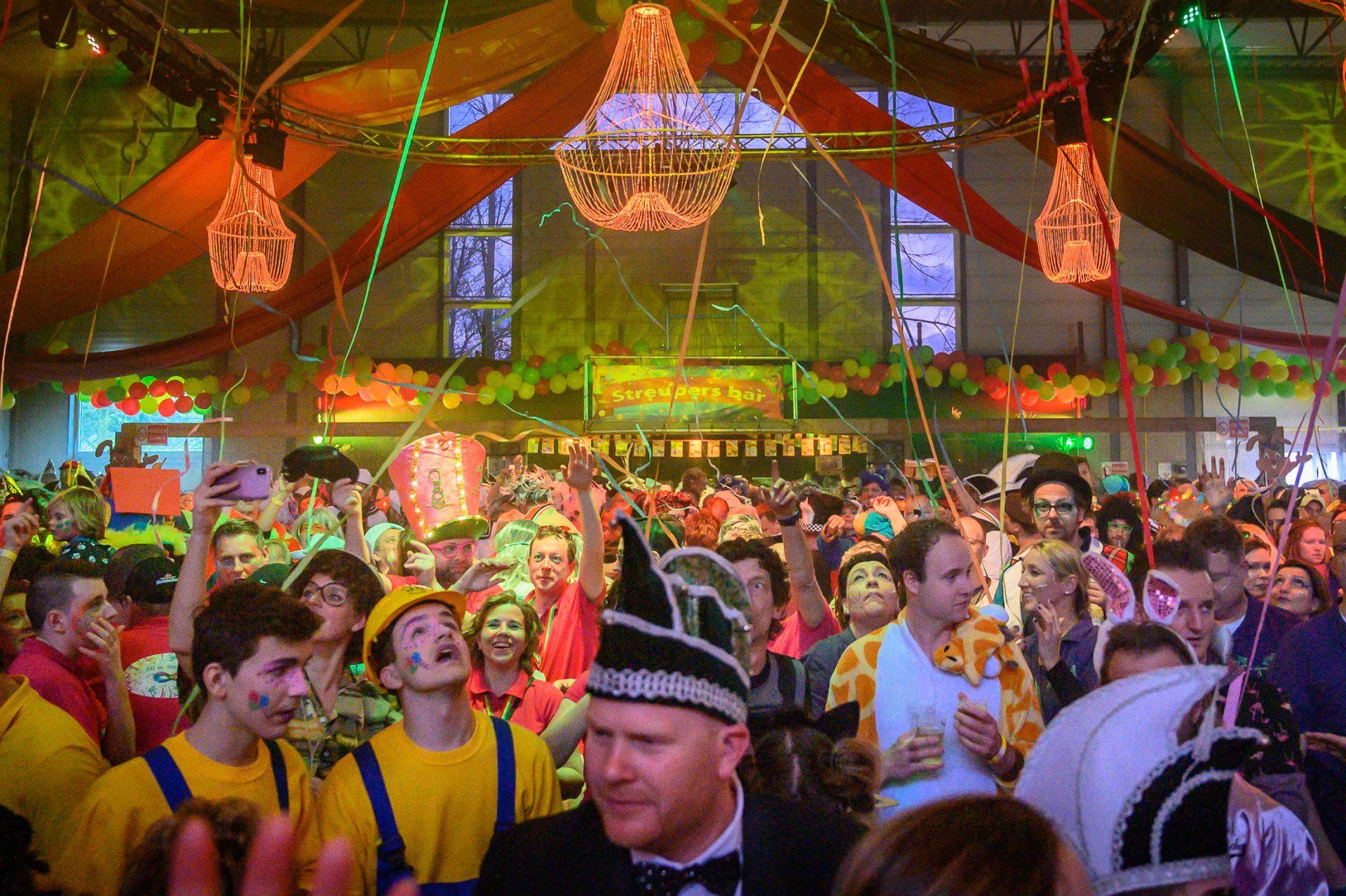 Een grote groep mensen verzamelt zich in een grote ruimte tijdens een kermis.