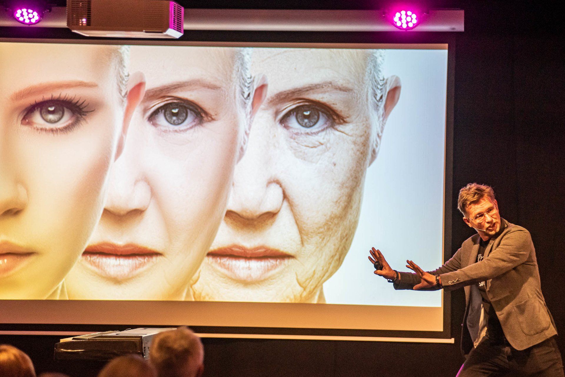 Een man geeft een presentatie voor een projectiescherm met daarop een afbeelding van het gezicht van een vrouw.