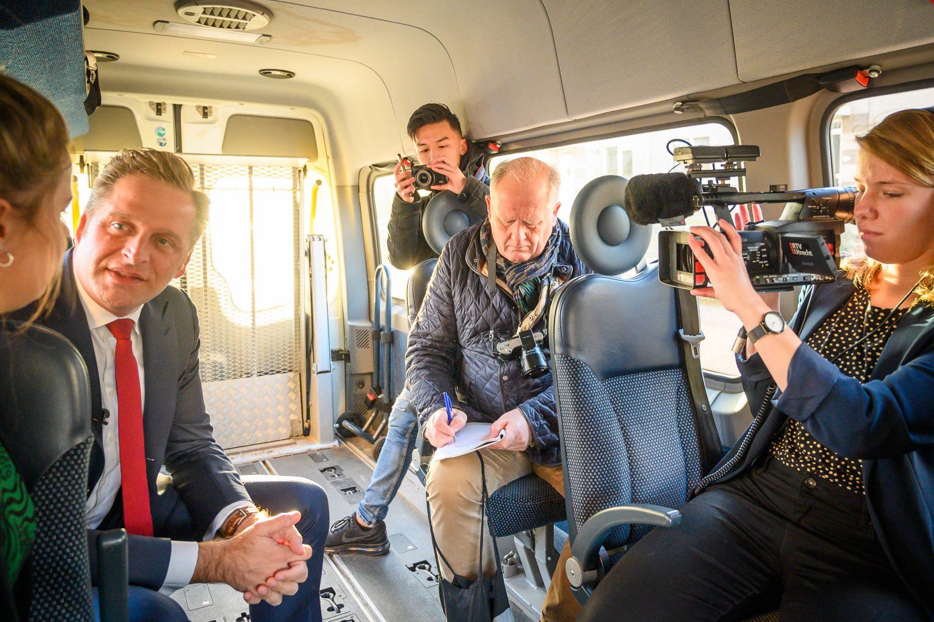 Een groep mensen zit in een busje en wordt geïnterviewd door een cameraman.