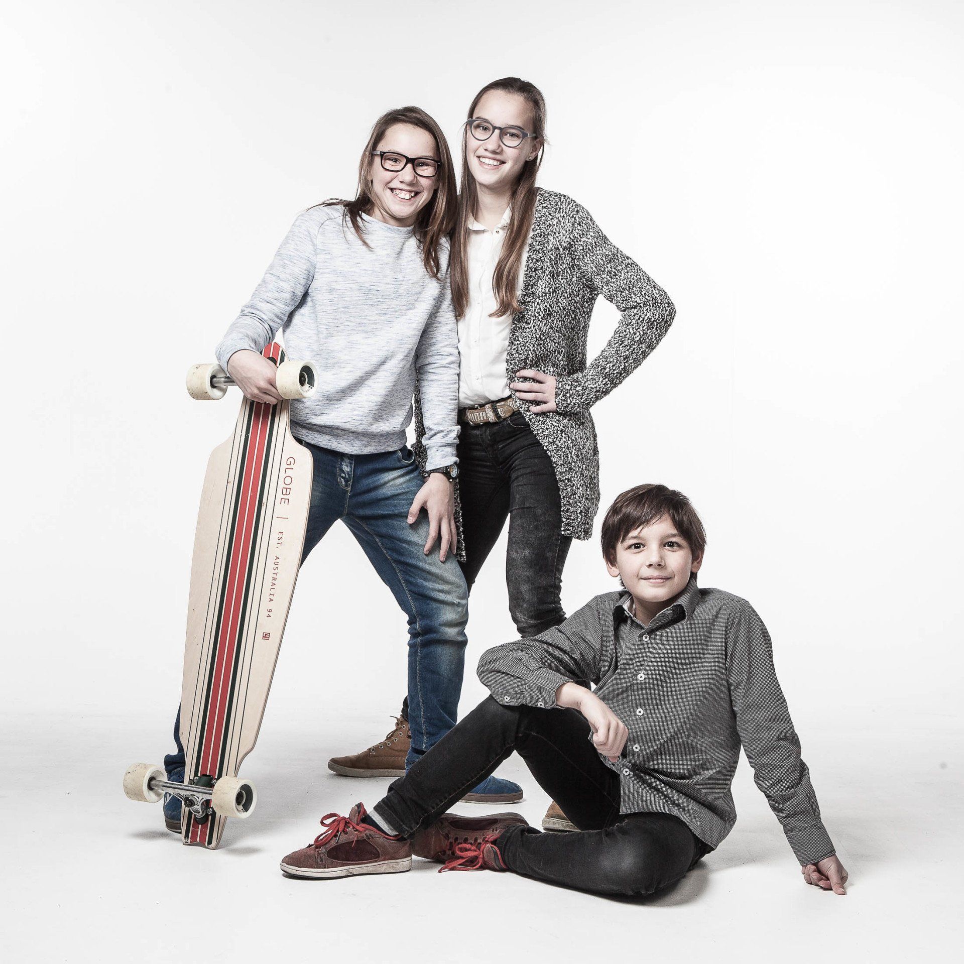 Twee meisjes en een jongen poseren voor een foto, terwijl een meisje een skateboard vasthoudt.