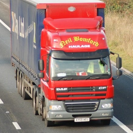 Red haulage lorry driving on a motorway beside a blue container truck