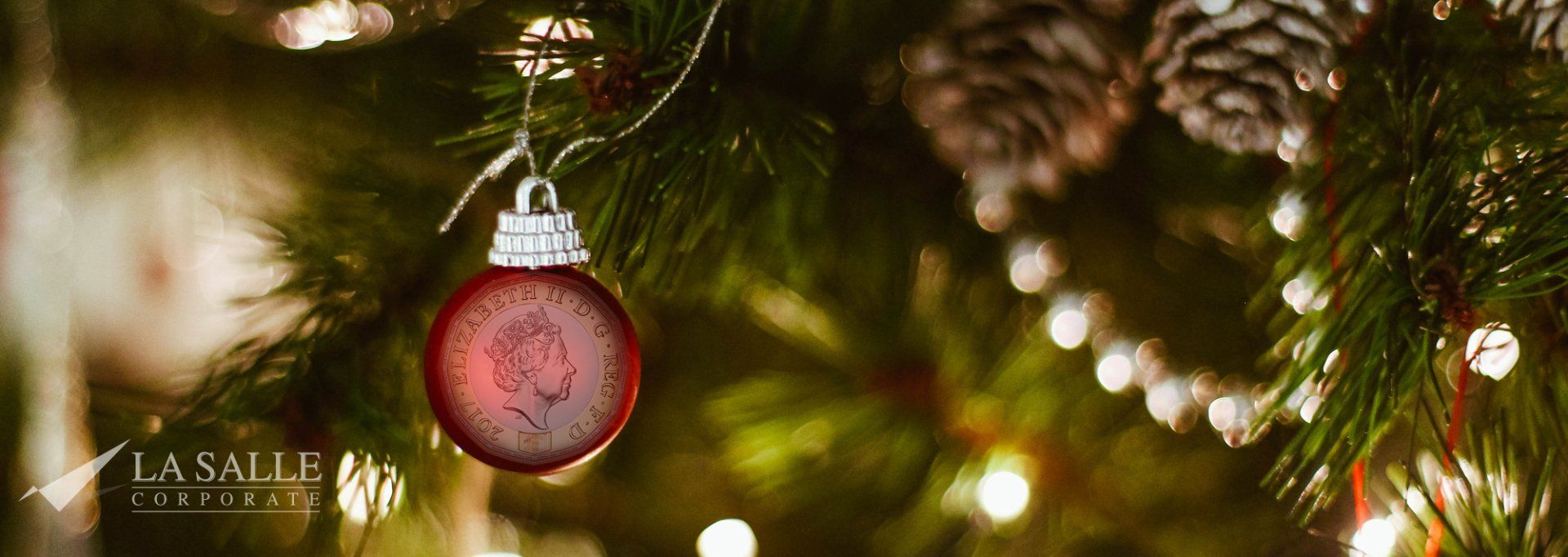 Close-up of a pink Christmas ornament hanging on a tree with warm lights and greenery