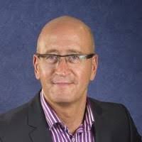 Man in glasses and dark blazer over striped shirt against a blue background