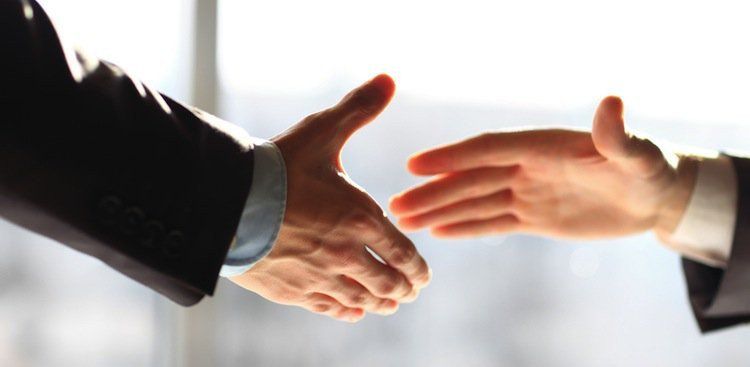 Two business people reaching out to shake hands against a bright white background