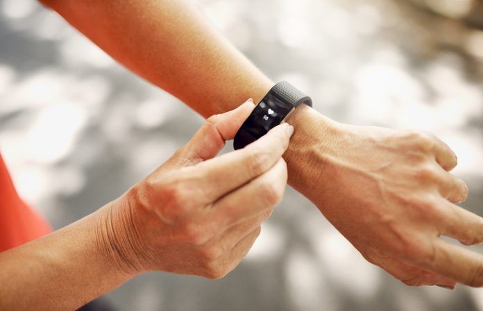 Hands fastening a black fitness tracker on a wrist outdoors