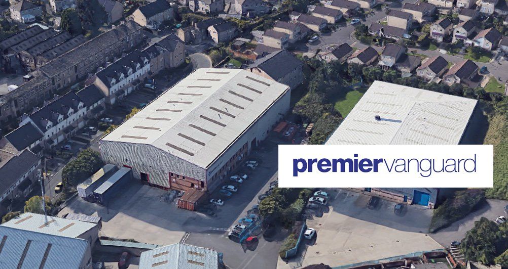 Aerial view of a large white-roofed commercial building in a suburban neighborhood, labeled “premiervanguard.”