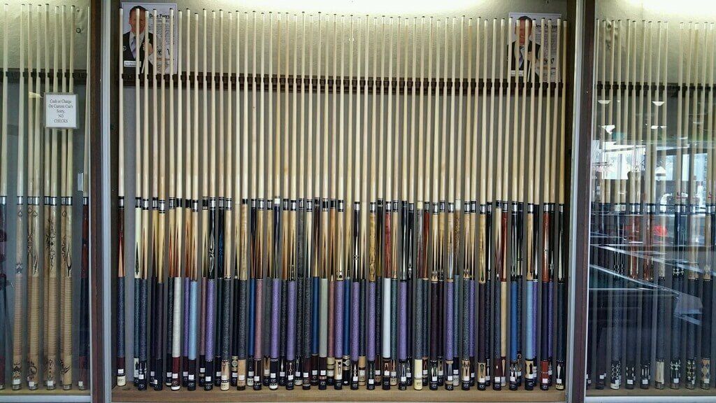 Racks of colorful pool cues displayed behind glass in a shop window
