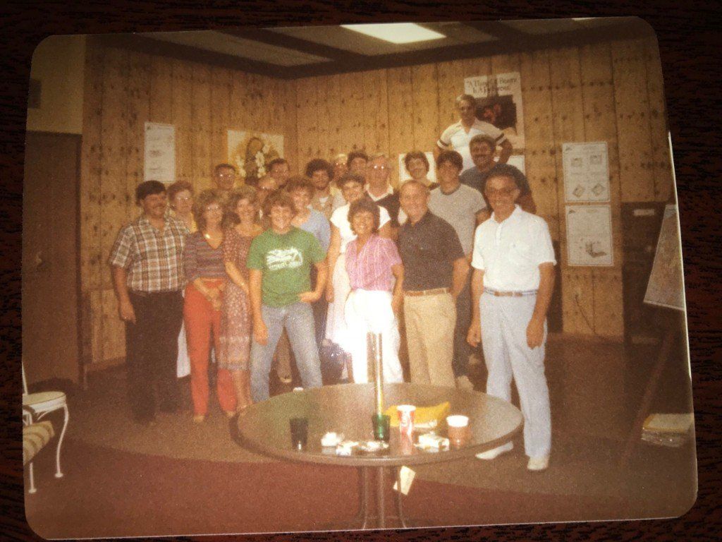 A group of people standing around a table with a man wearing a green shirt that says catch
