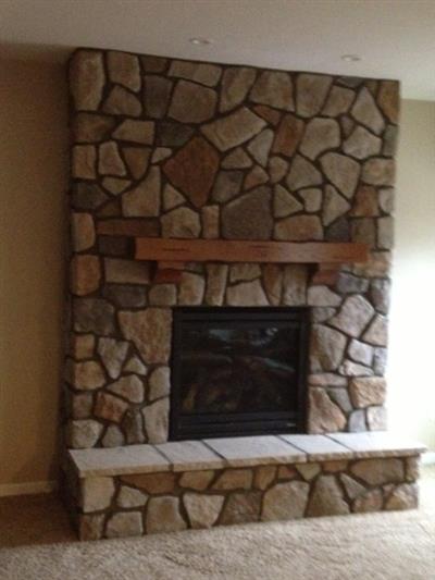 A stone fireplace with a wooden mantle in a living room