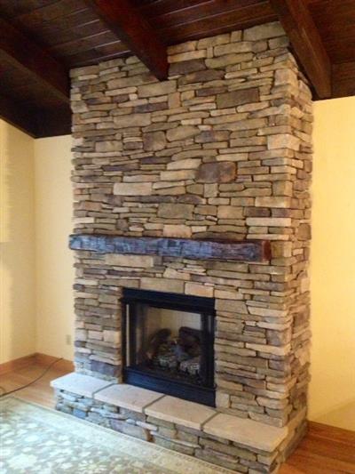 A large stone fireplace in a living room with a wooden ceiling.