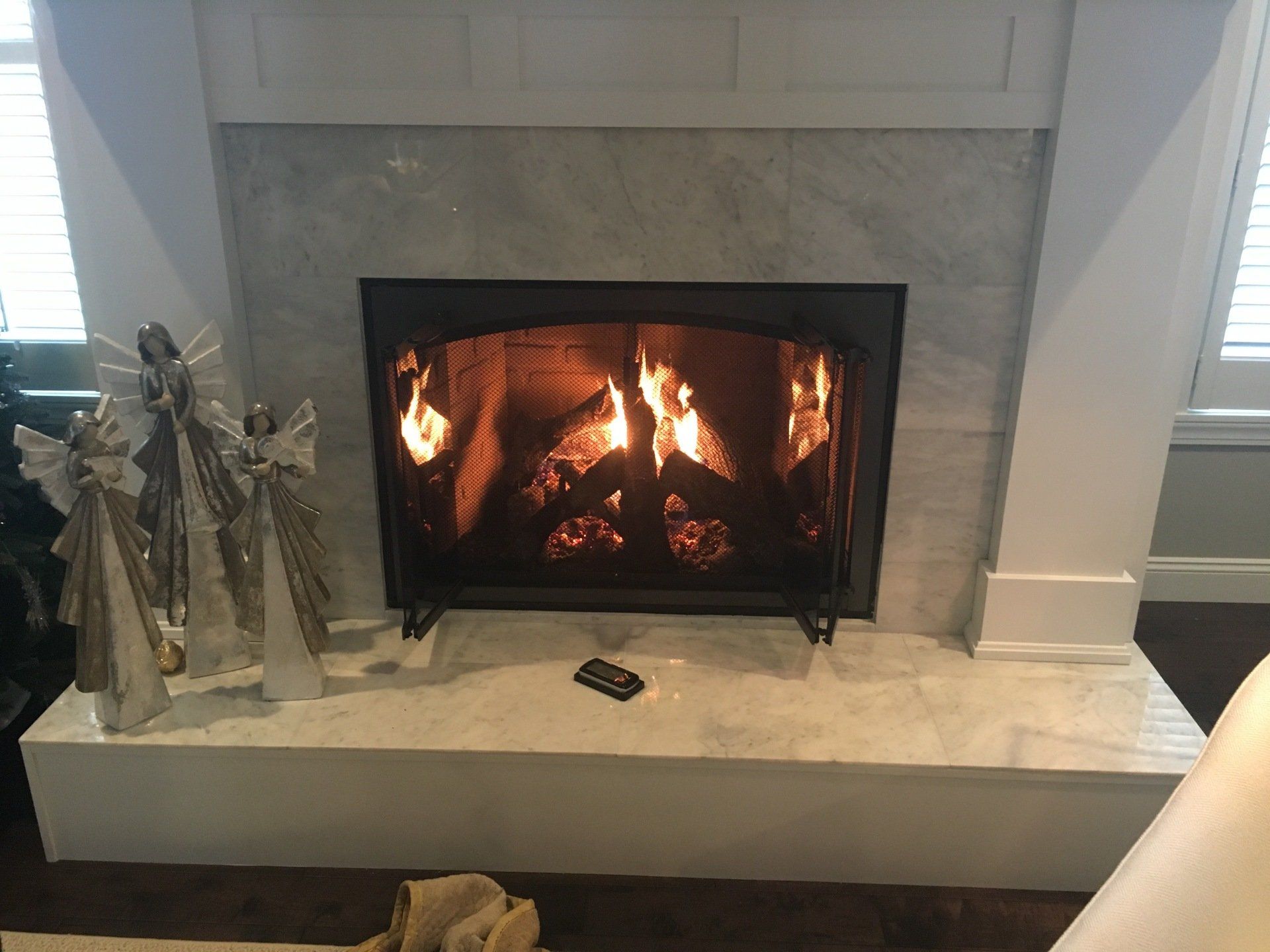 Fireplace with burning flames, white marble, decorative angels, and a remote.