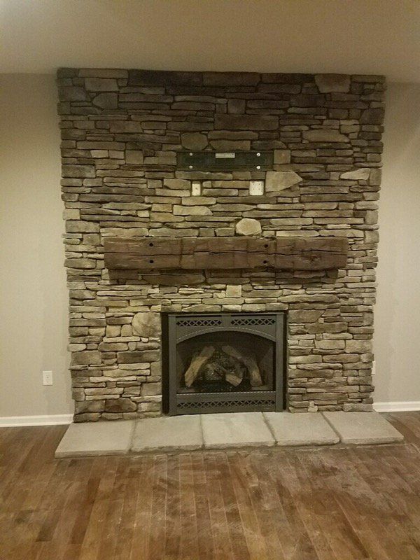 A fireplace with a stone wall and a wooden mantle in a living room.