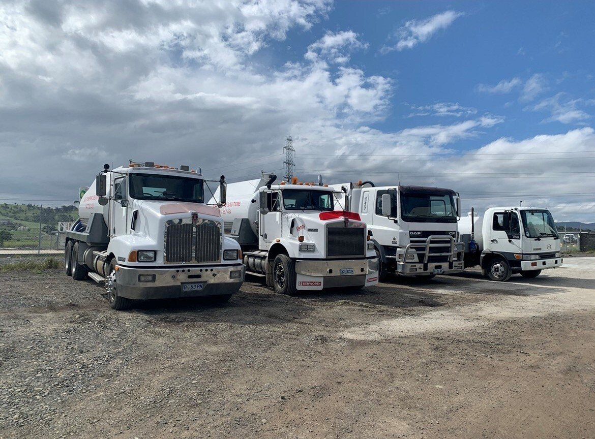 Four white trucks parked on gravel under a partly cloudy sky.
