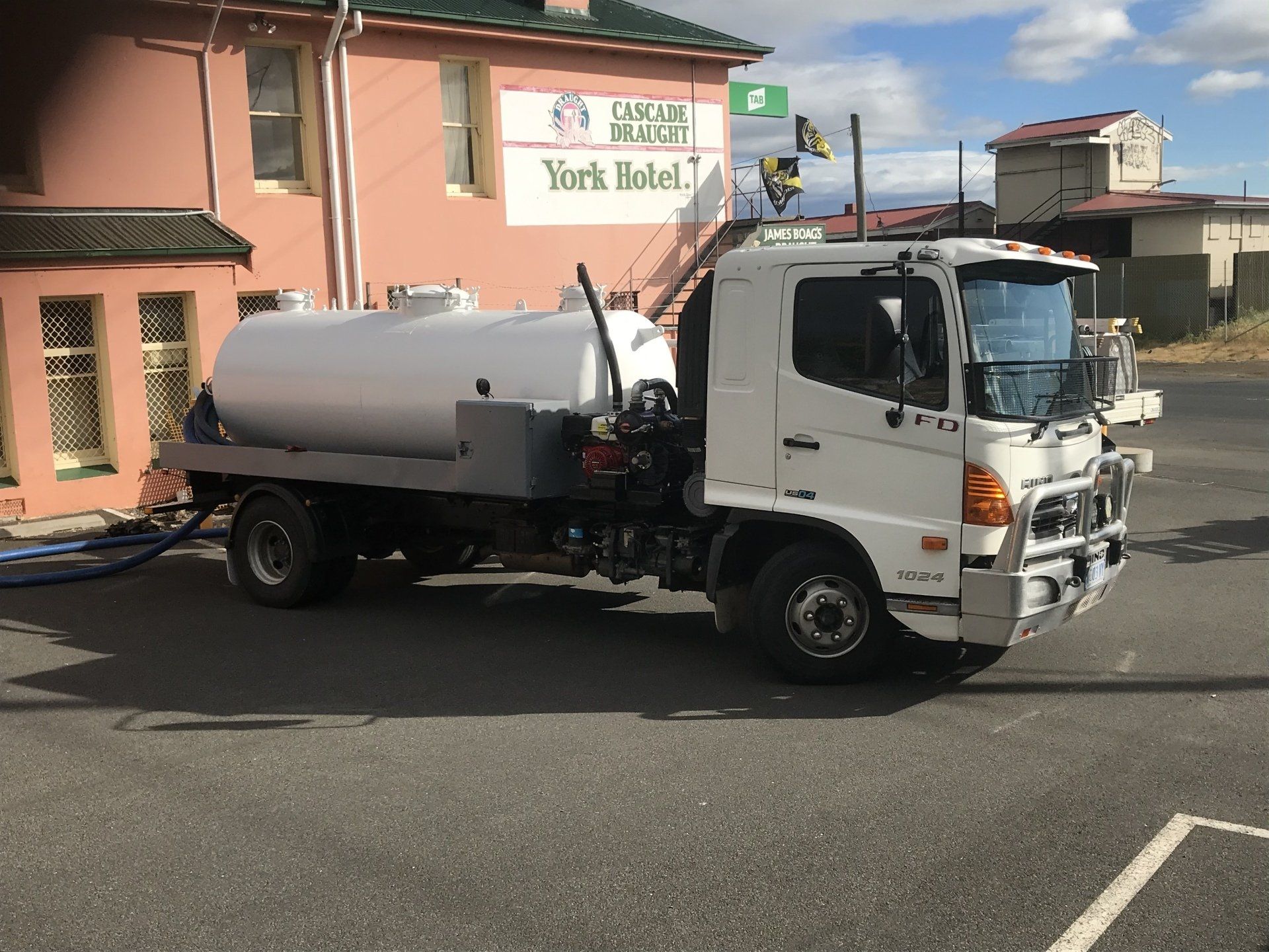 White tanker truck parked outside the York Hotel in Australia. Blue hose runs from the truck to the building.