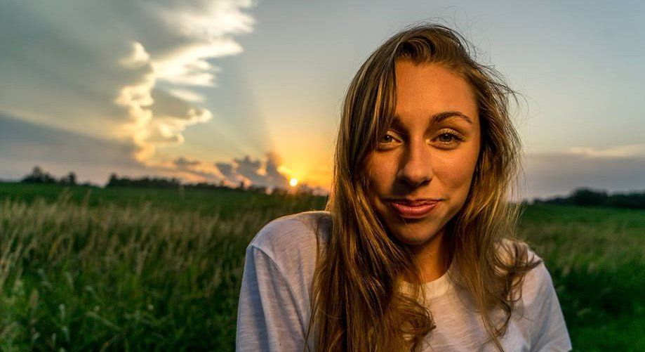 A woman is standing in a field with a sunset in the background.
