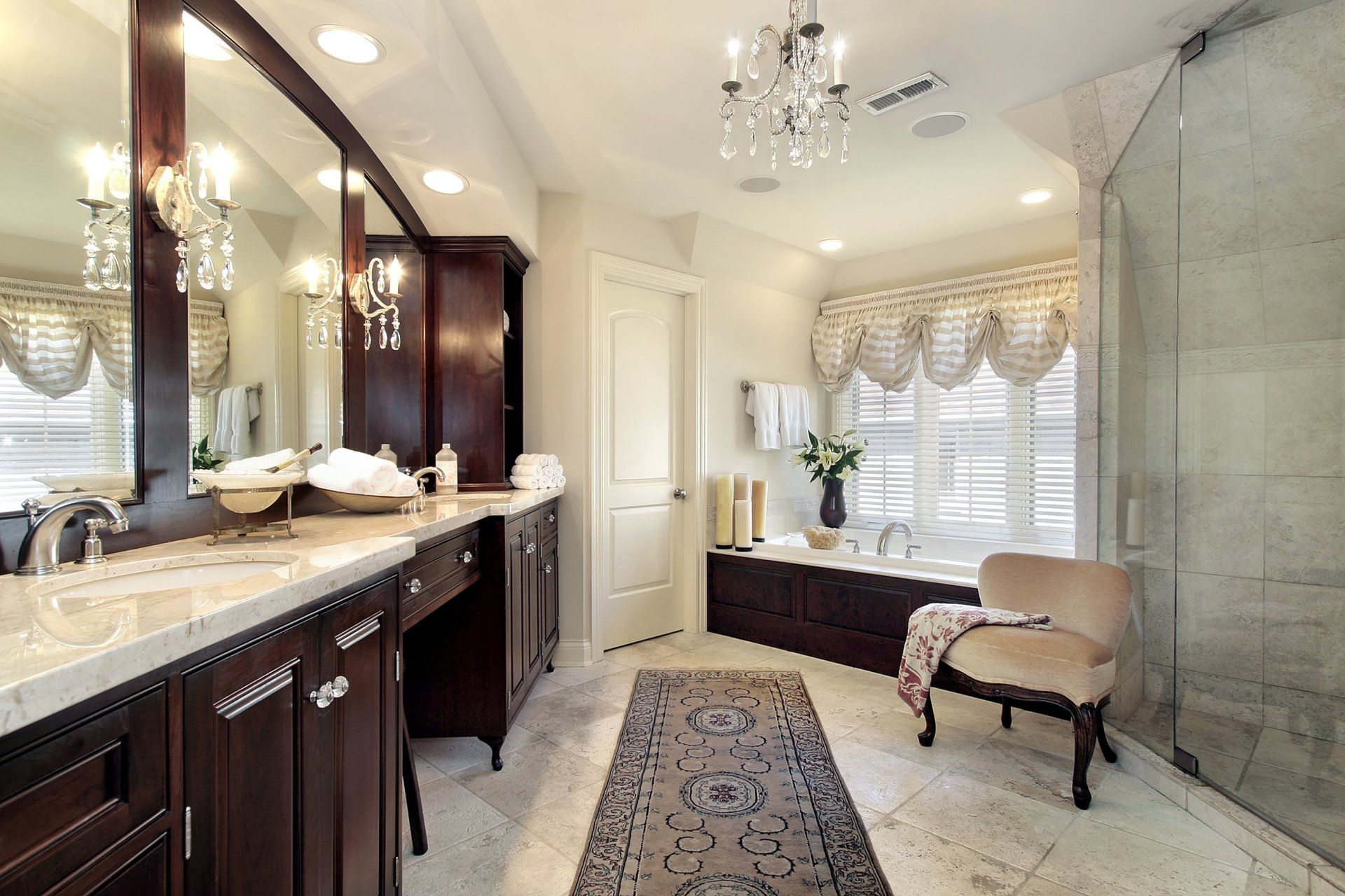 A bathroom with two sinks , a chair , and a walk in shower.