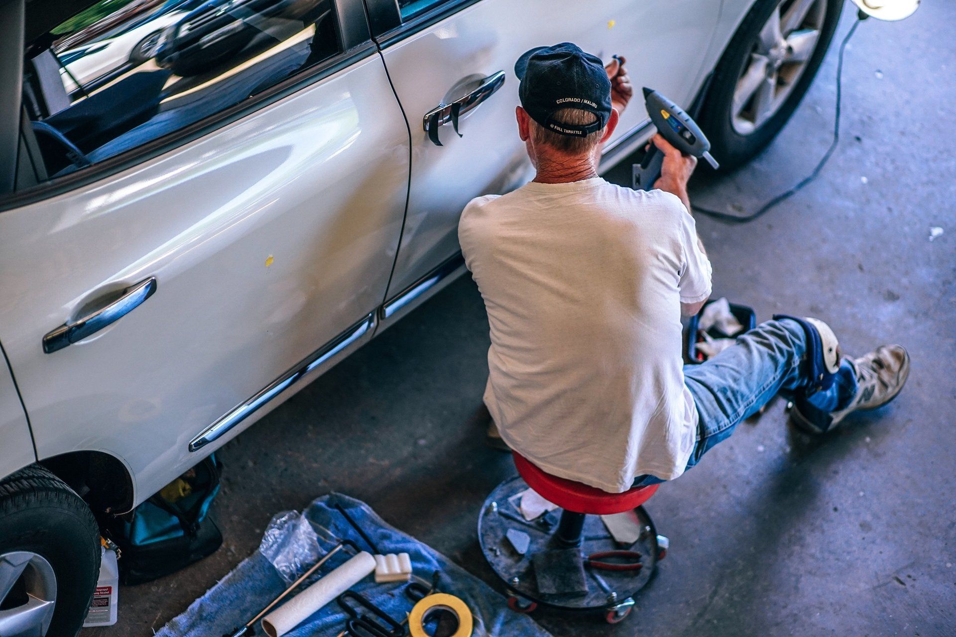 a man is sitting on a stool working on a car in a garage .