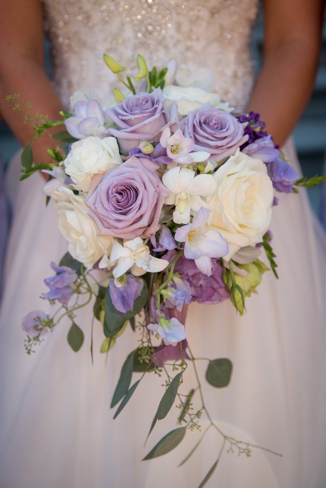 a bride in a white dress is holding a bouquet of purple and white flowers .