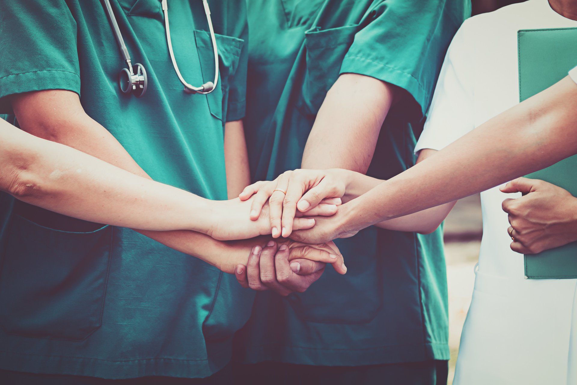 A group of doctors and nurses are putting their hands together.