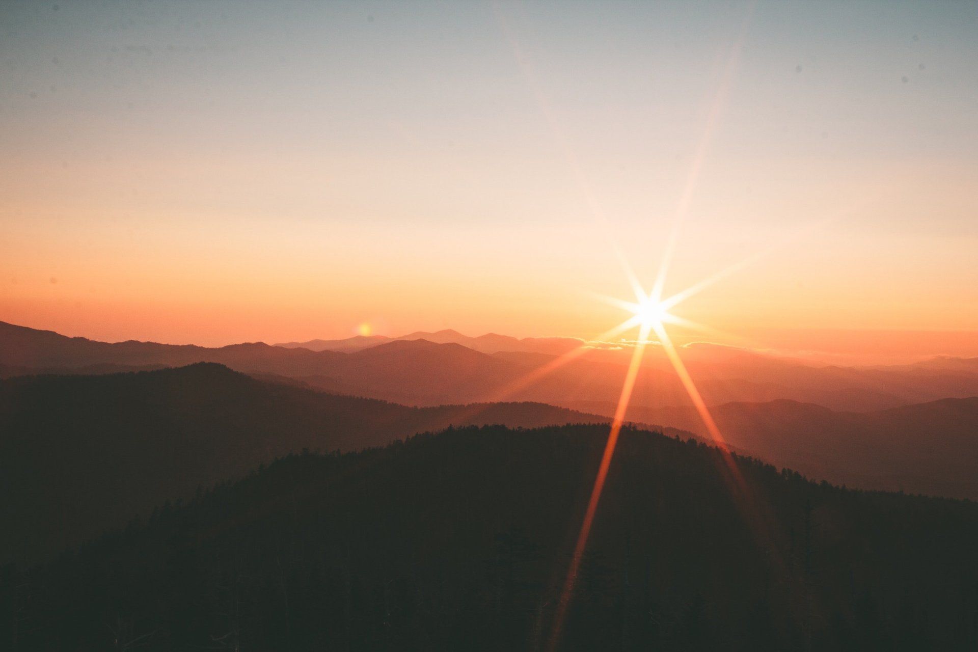 The sun is shining brightly over the mountains at sunset.