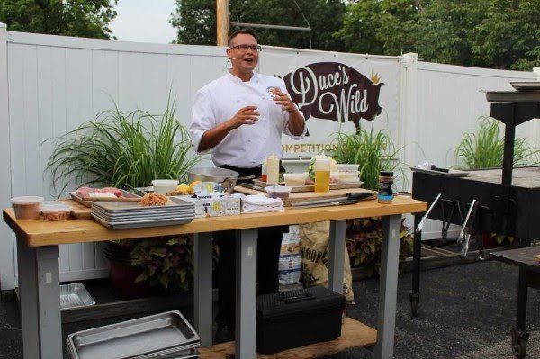 A man is standing in front of a table with a sign that says duces wild on it.