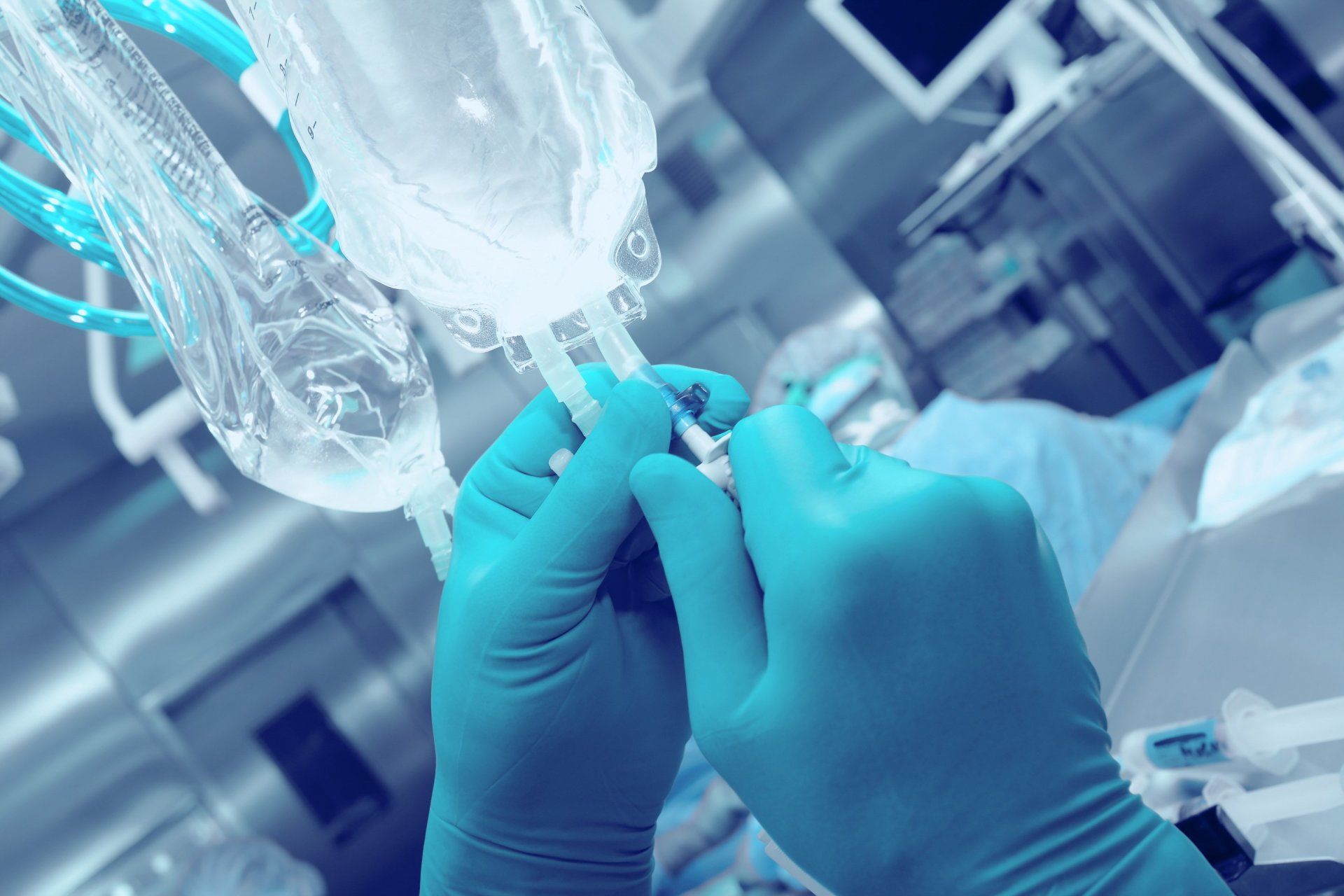 A person wearing blue gloves is holding a syringe in a hospital room.
