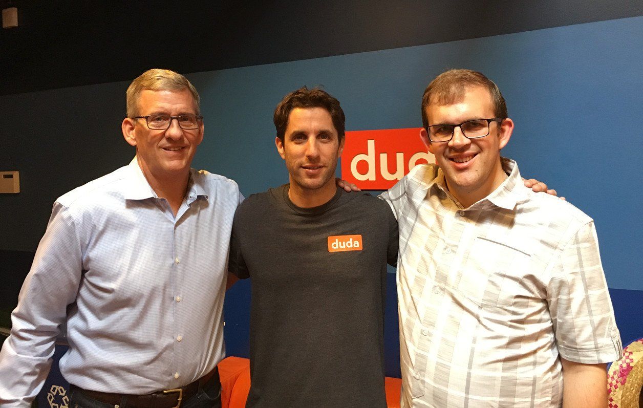 Three men are posing for a picture in front of a sign that says due