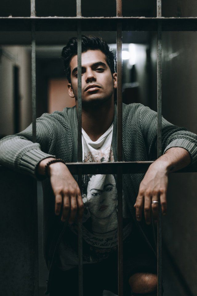 A man is sitting behind bars in a prison cell.