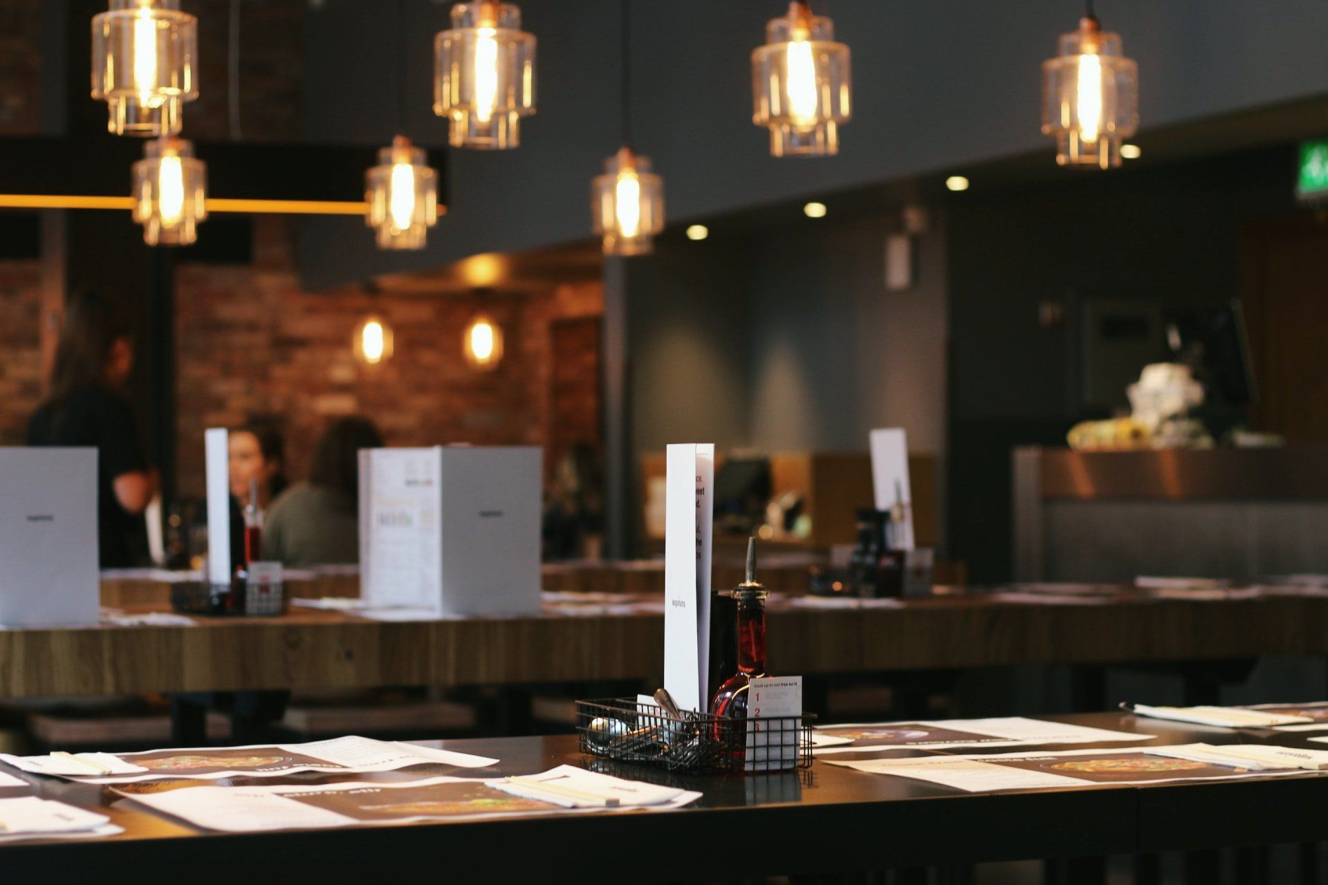 A restaurant with a lot of tables and lamps hanging from the ceiling.