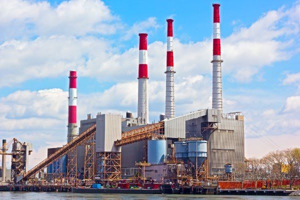 A power plant with red and white chimneys next to a body of water.