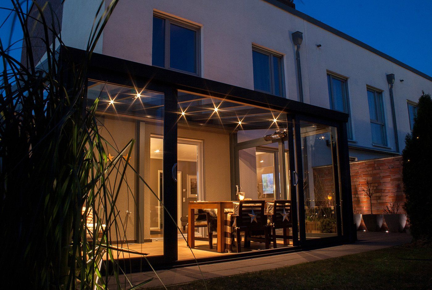 Ein Haus mit einer überdachten Terrasse, vor der nachts ein Tisch und Stühle stehen.