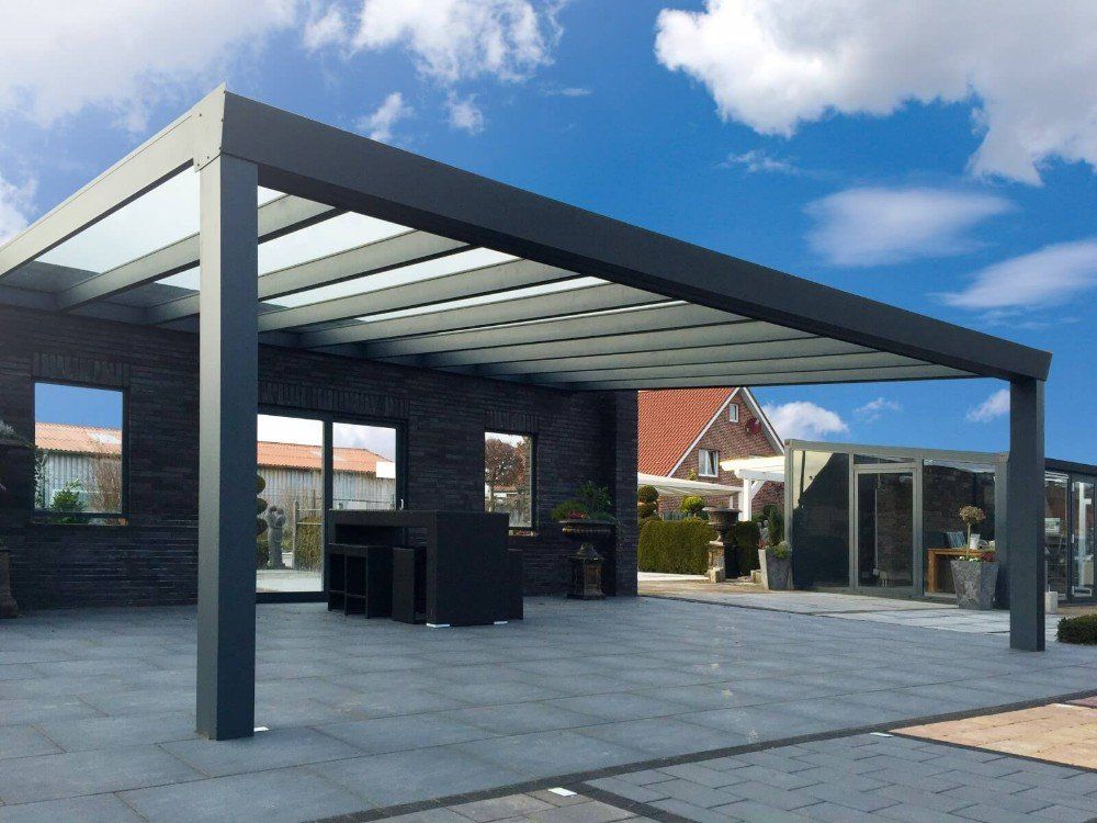 Auf einer Terrasse vor einem Haus steht eine Pergola mit Glasdach.