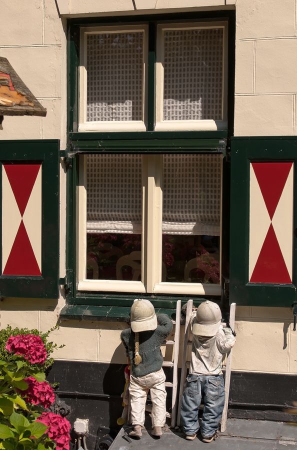 Twee beeldjes van kinderen die onder een raam met rode en witte luiken een ladder beklimmen.