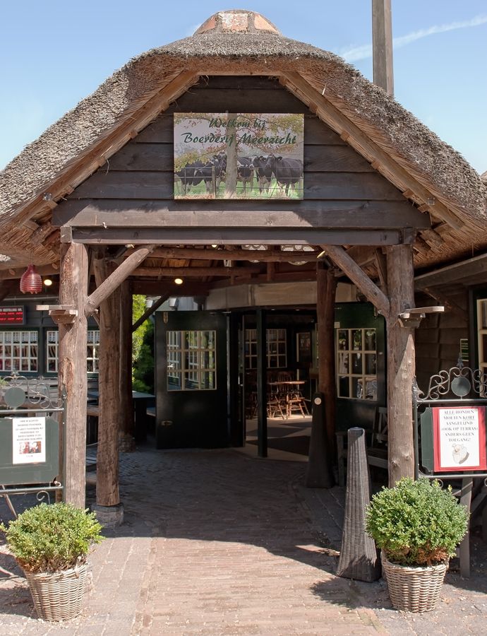 Ingang van een winkel met een rieten dak, houten balken en een uithangbord met twee schapen.