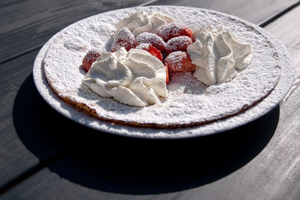 Een pannenkoek met aardbeien, slagroom en poedersuiker, geserveerd op een wit bord.