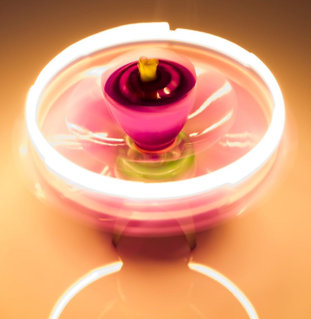 Een ronddraaiende roze en groene tol met een wit oplichtende ring, die door beweging wazig wordt.