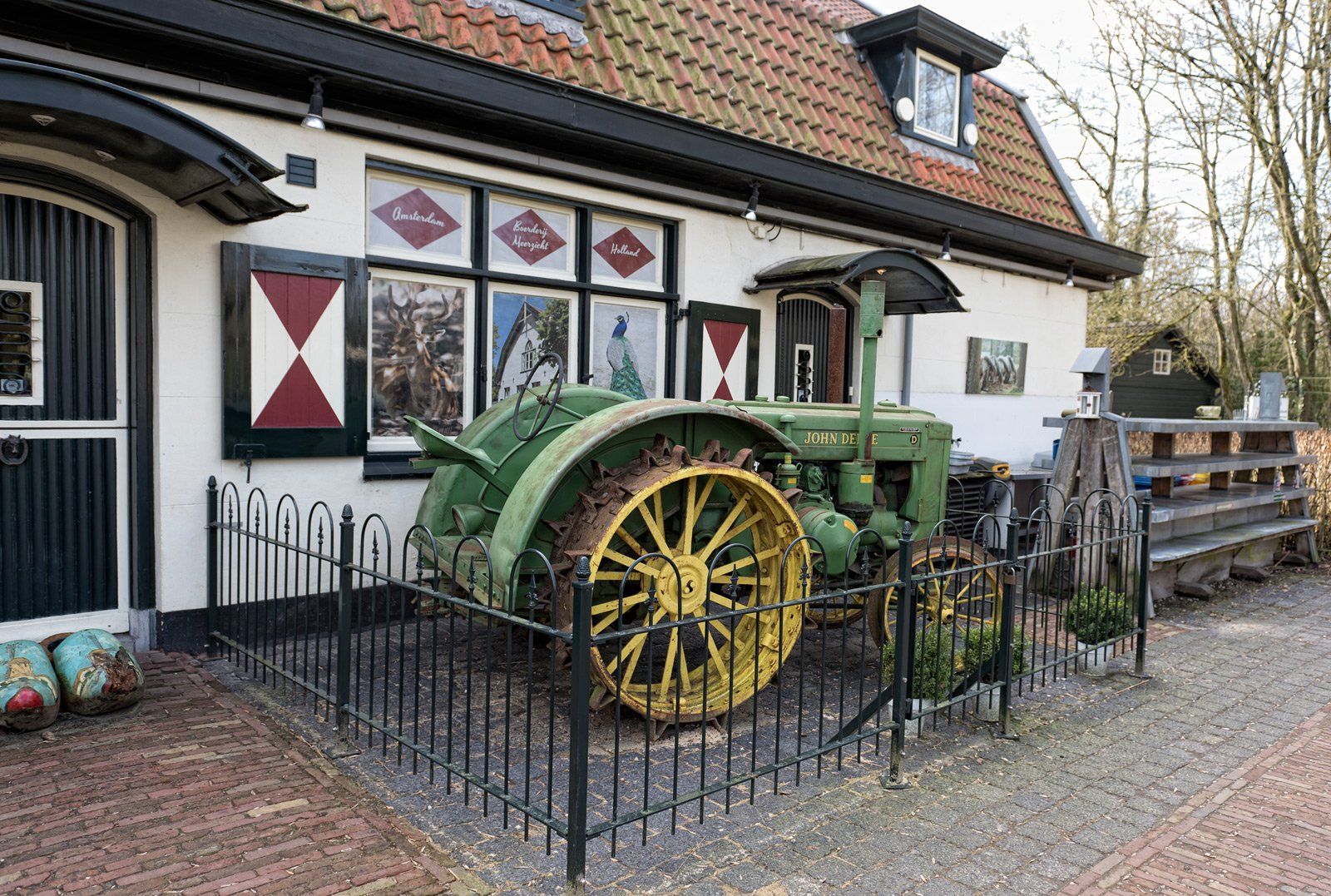 Een groene en gele tractor staat tentoongesteld voor een wit gebouw met zwarte luiken en een rood pannendak.