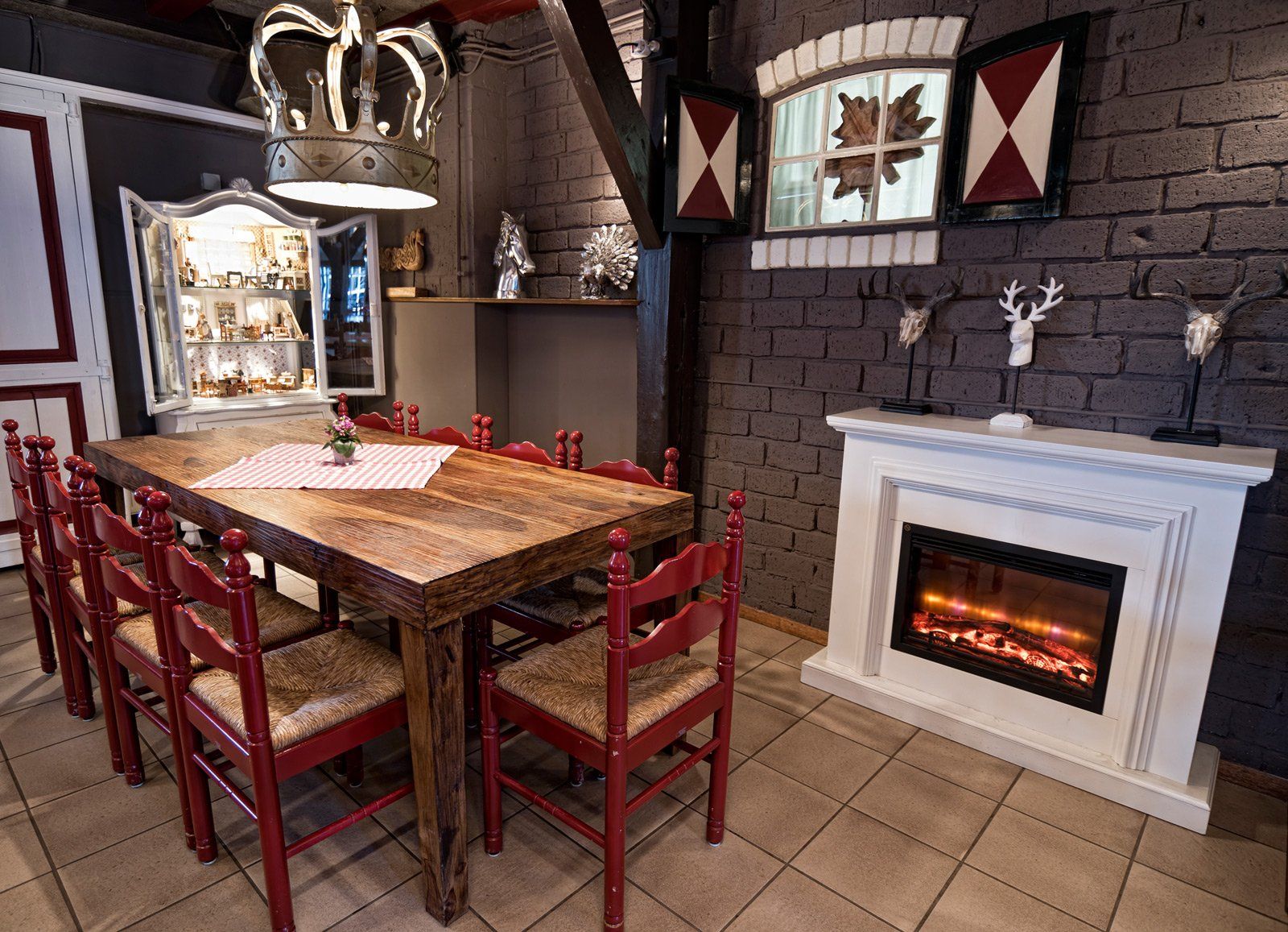 Eetkamer met houten tafel en rode stoelen, open haard en decoratieve kroonlamp.