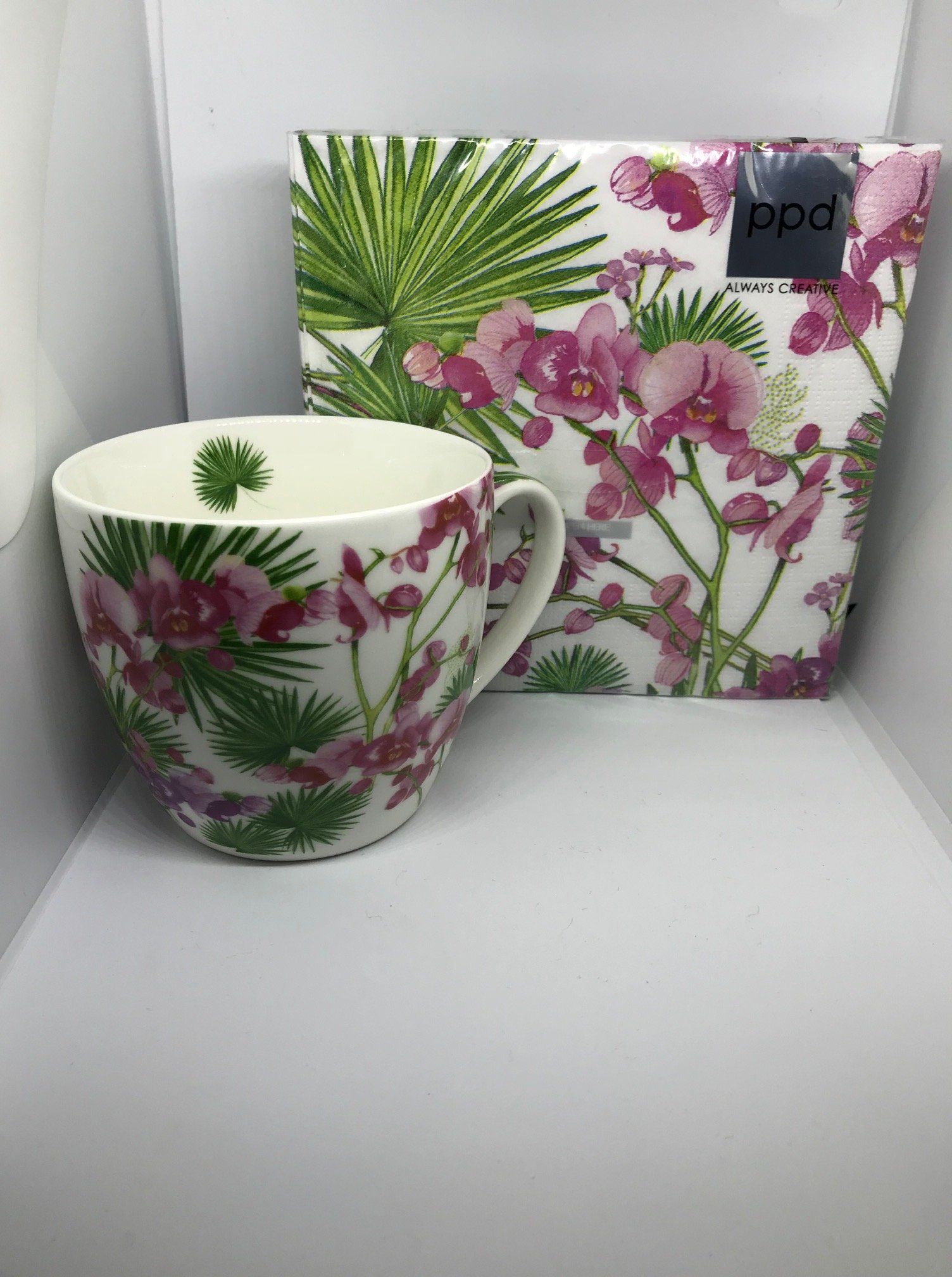 Witte mok met roze orchidee en groene bladeren, naast een bijpassende geschenkdoos.