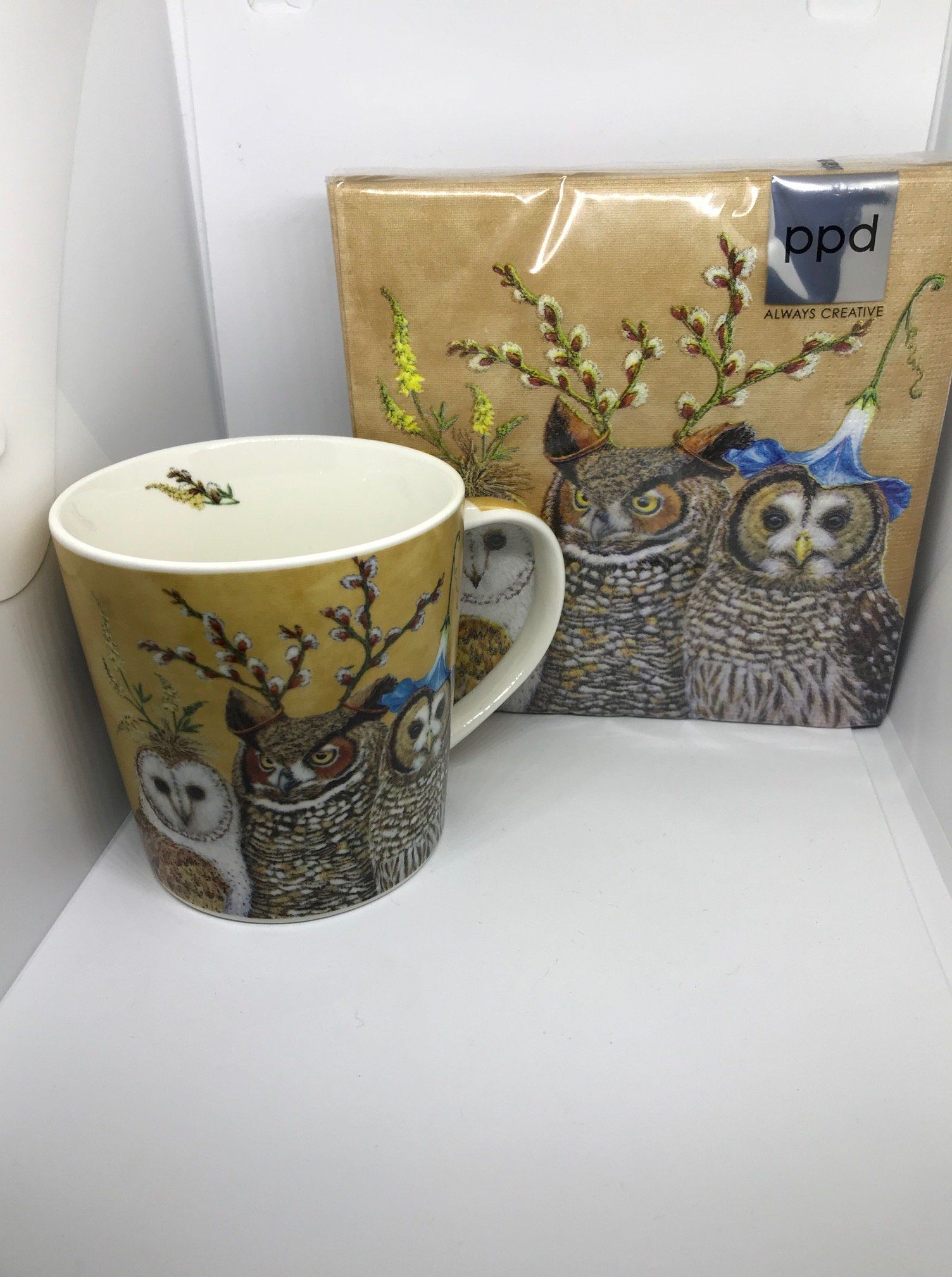 Een set bestaande uit een mok en een bijpassend papieren servet met uilenmotief op een witte achtergrond. De mok is versierd met afbeeldingen van uilen en bloemen.
