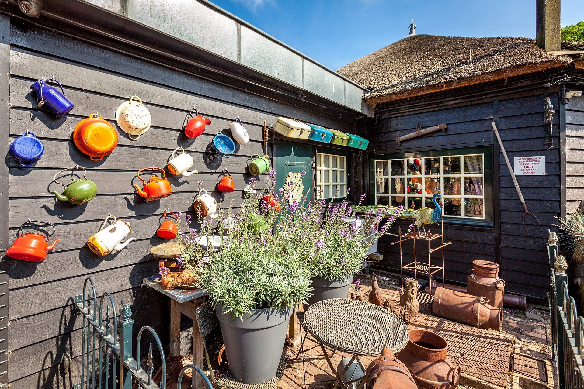 Zwart houten gebouw met kleurrijke theepotten, potplanten en vintage decoratie.