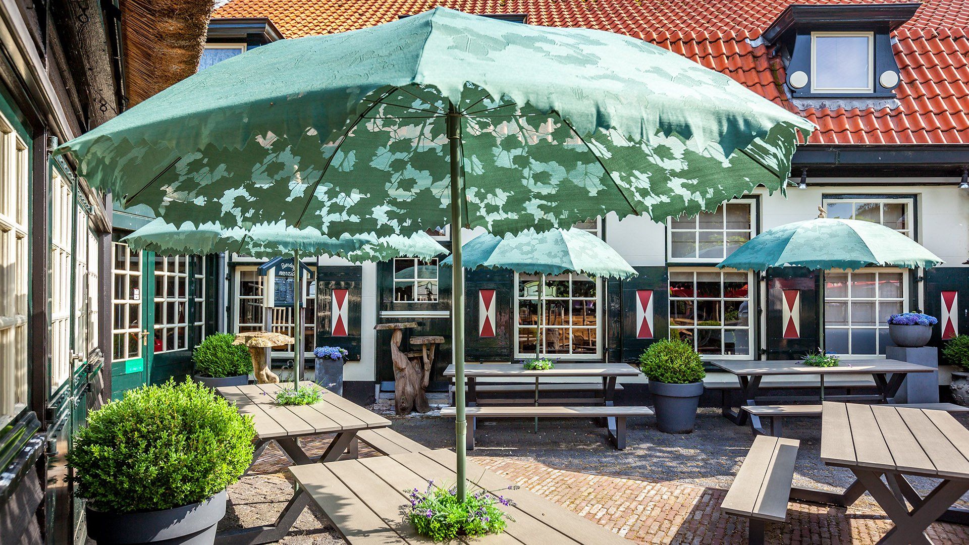 Terras van een restaurant met groene parasols, houten tafels en potplanten.