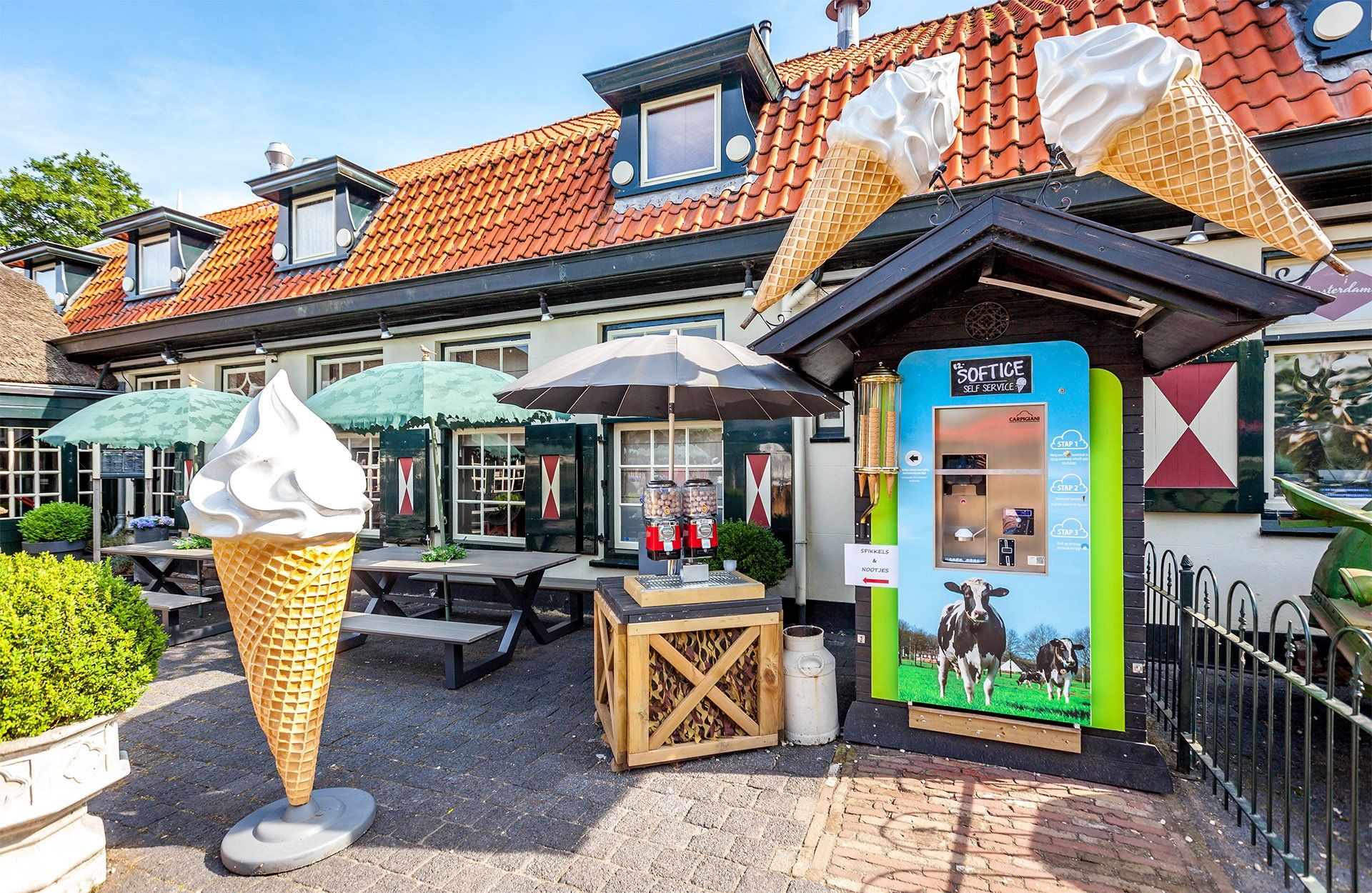 Een ijssalon met een gigantisch ijshoorntje als beeld, een terras en een melkautomaat.