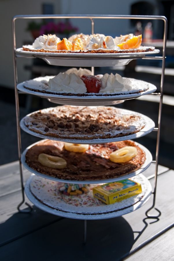 Pannenkoeken op een etagère; belegd met slagroom, fruit en kruimels. Buiten, op een tafel.