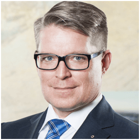 Ein Mann mit Brille, Anzug und Krawatte lächelt in die Kamera.