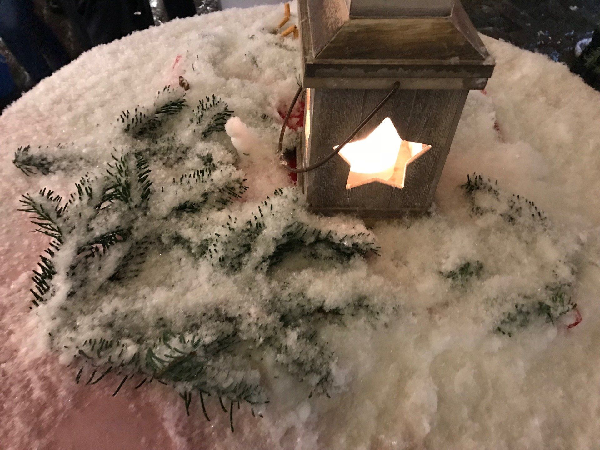 Eine Laterne mit einem Stern in der Mitte steht auf einem schneebedeckten Tisch.