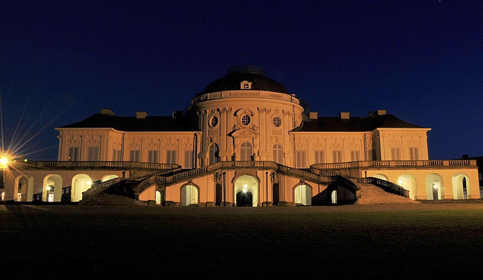 Ein großes Gebäude mit Bögen und Treppen ist nachts beleuchtet.