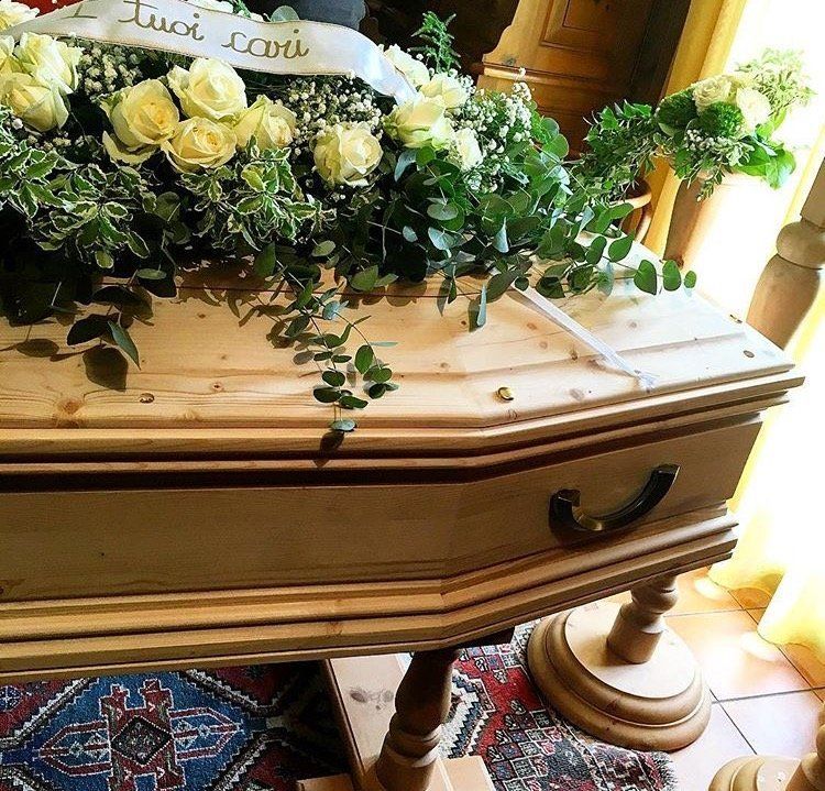 Una bara di legno con fiori sopra e un nastro con la scritta 