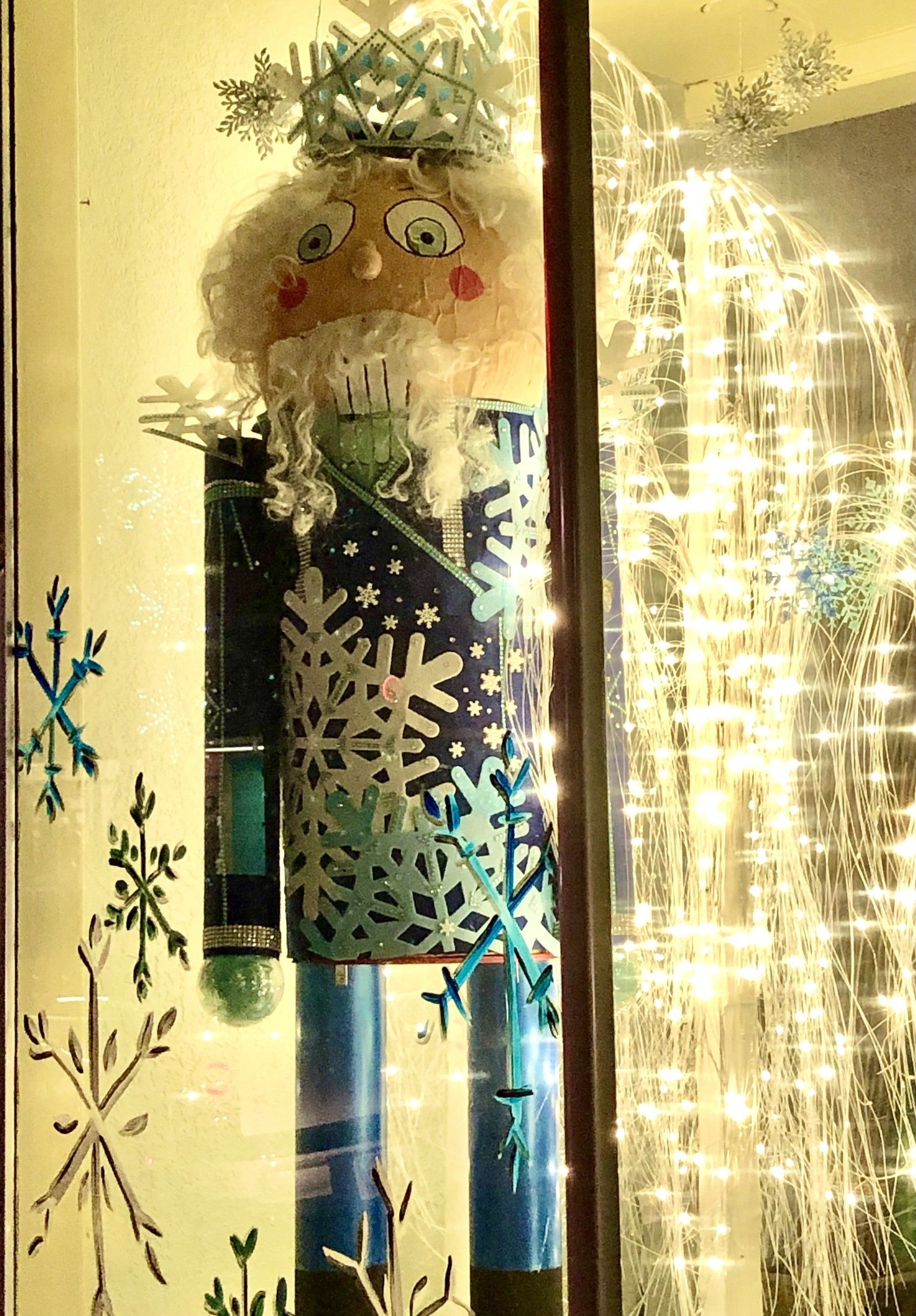 A nutcracker is sitting in a window next to a christmas tree.